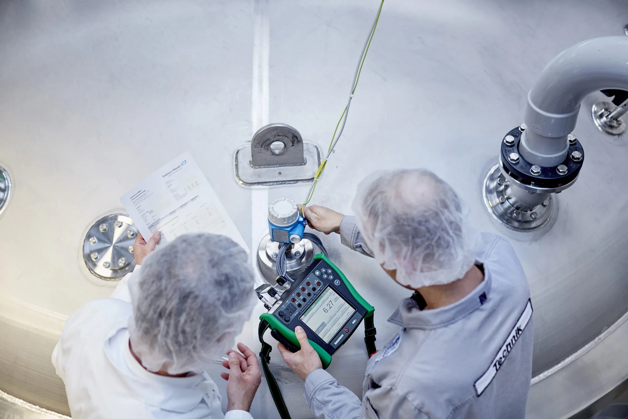 ACI technicians calibrating a pressure transmitter on a stainless-steel process vessel with a documenting calibrator