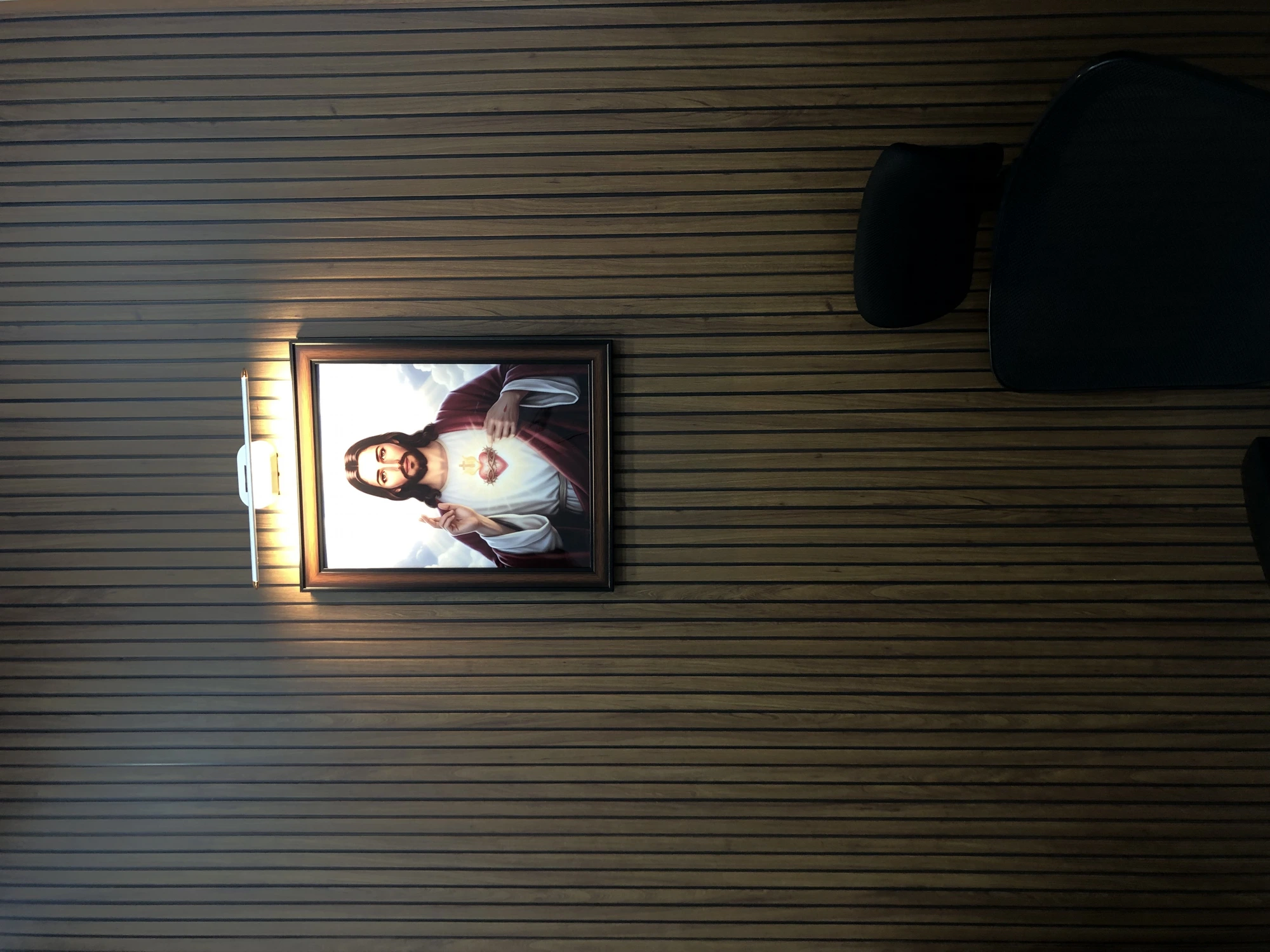 Framed Sacred Heart portrait, spot-lit on the slat wall