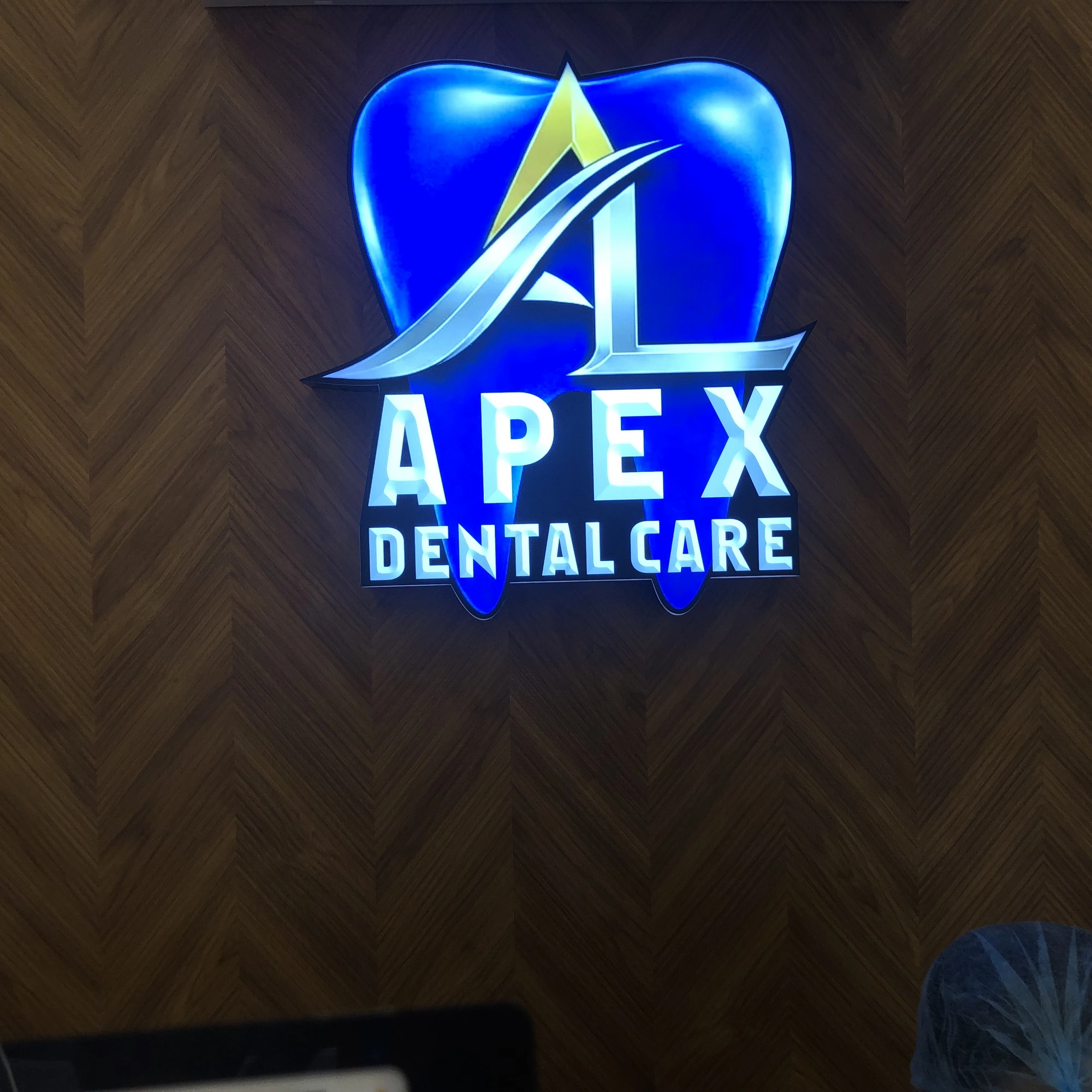 Backlit Apex Dental Care logo on herringbone wood panel